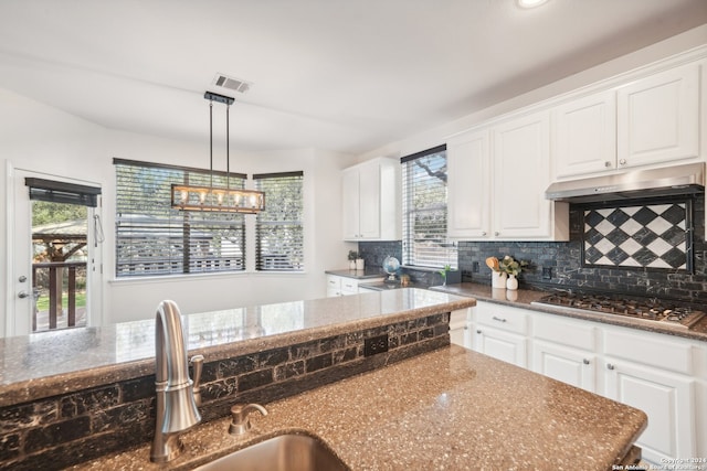 kitchen with white cabinets, hanging light fixtures, sink, stainless steel gas stovetop, and dark stone countertops