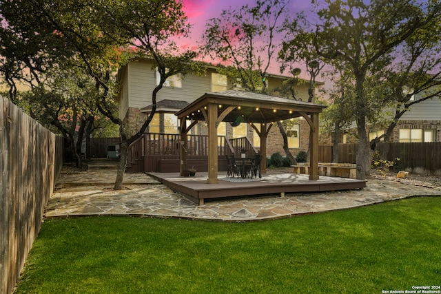 back house at dusk with a gazebo, a lawn, and a wooden deck