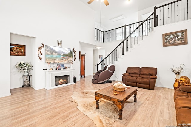 living area featuring wood finished floors, stairs, a glass covered fireplace, ceiling fan, and a high ceiling