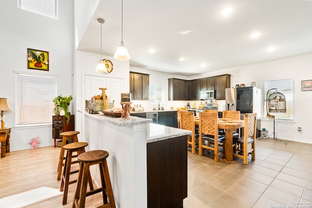 kitchen with light stone countertops, a breakfast bar, dark brown cabinetry, stainless steel appliances, and pendant lighting