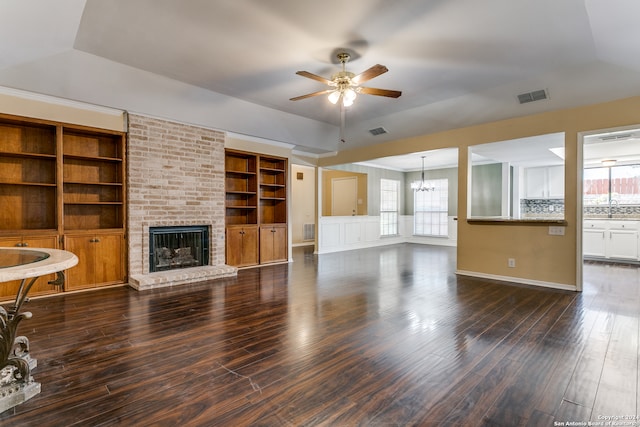 unfurnished living room featuring ceiling fan with notable chandelier, a fireplace, plenty of natural light, and dark hardwood / wood-style floors