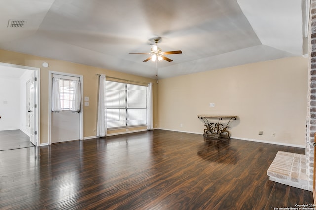 unfurnished living room with ceiling fan, a tray ceiling, dark hardwood / wood-style floors, and vaulted ceiling