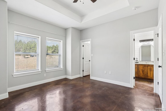 unfurnished bedroom featuring a raised ceiling, connected bathroom, and ceiling fan