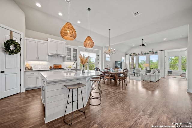 kitchen featuring ceiling fan with notable chandelier, a breakfast bar, a center island with sink, lofted ceiling, and white cabinets