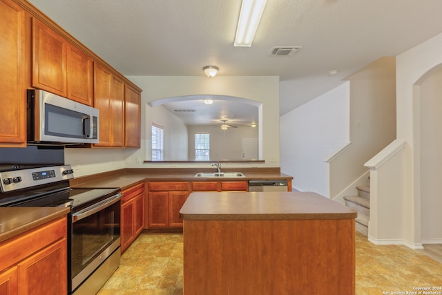 kitchen with stainless steel appliances, a kitchen island, sink, and ceiling fan