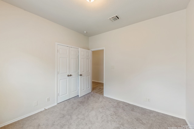 unfurnished bedroom with a closet and light colored carpet