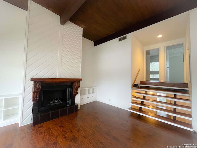 unfurnished living room with beamed ceiling, dark wood-type flooring, a tile fireplace, and wooden ceiling