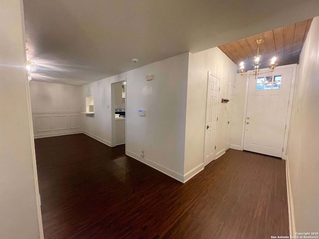 hallway featuring dark hardwood / wood-style floors, wooden ceiling, and a chandelier