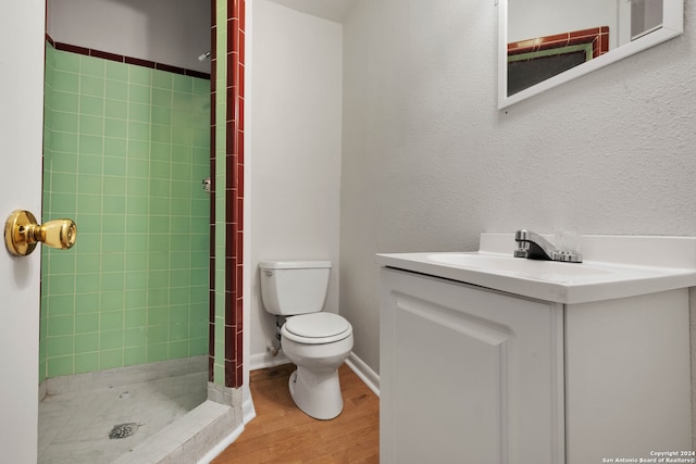 bathroom featuring a tile shower, hardwood / wood-style flooring, vanity, and toilet