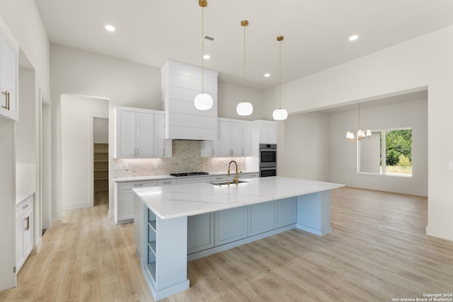 kitchen featuring pendant lighting, light hardwood / wood-style floors, white cabinets, and a kitchen island with sink