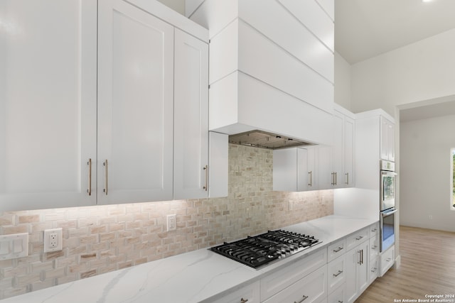 kitchen featuring white cabinets, light hardwood / wood-style flooring, appliances with stainless steel finishes, light stone countertops, and decorative backsplash