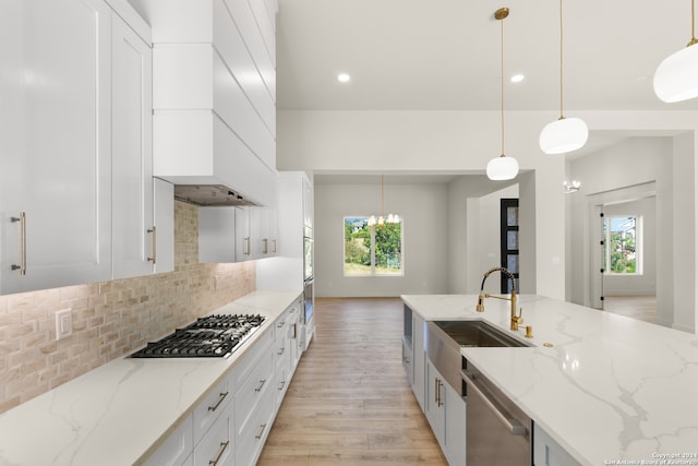 kitchen with light stone counters, sink, light hardwood / wood-style floors, appliances with stainless steel finishes, and decorative light fixtures