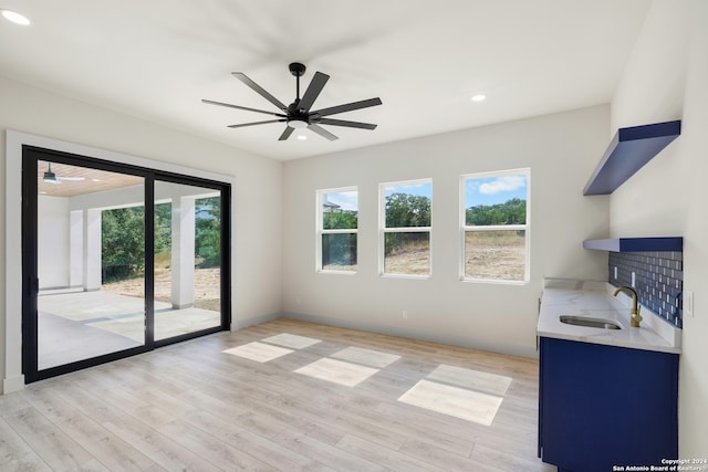 unfurnished living room with ceiling fan, light hardwood / wood-style flooring, sink, and a healthy amount of sunlight