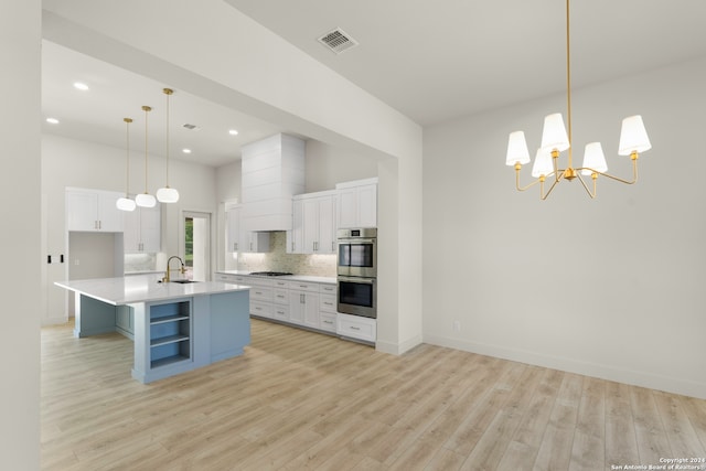 kitchen featuring an island with sink, light wood-type flooring, decorative light fixtures, and white cabinetry