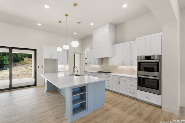 kitchen with an island with sink, decorative light fixtures, white cabinetry, stainless steel appliances, and light hardwood / wood-style floors