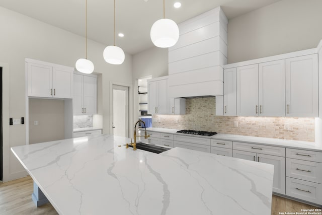 kitchen with light stone counters, white cabinets, gas stovetop, sink, and decorative light fixtures