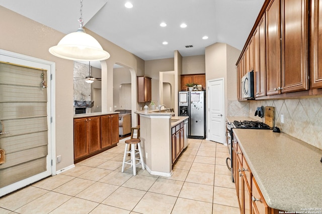 kitchen with ceiling fan, hanging light fixtures, a center island with sink, stainless steel appliances, and a kitchen breakfast bar