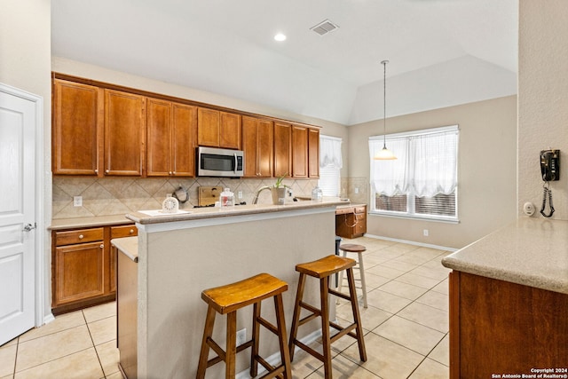 kitchen with a kitchen breakfast bar, hanging light fixtures, vaulted ceiling, light tile patterned floors, and backsplash