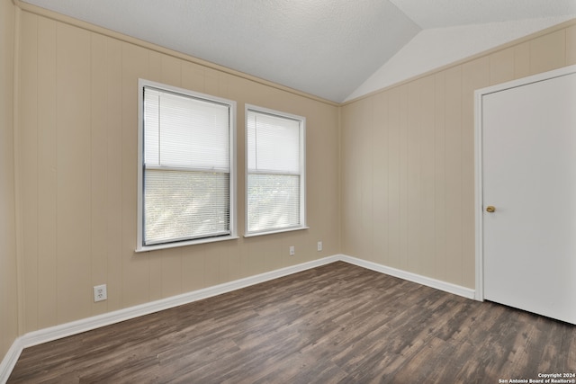 empty room featuring lofted ceiling, dark wood-type flooring, wooden walls, and a textured ceiling