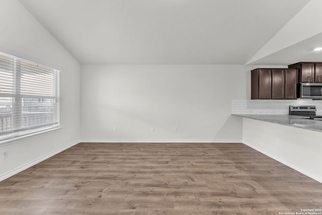 interior space featuring light stone counters, stainless steel appliances, dark brown cabinets, vaulted ceiling, and light hardwood / wood-style floors