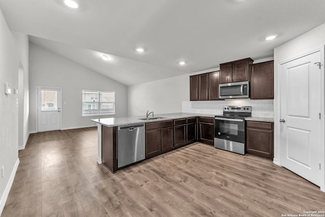 kitchen with light wood-type flooring, kitchen peninsula, vaulted ceiling, and stainless steel appliances