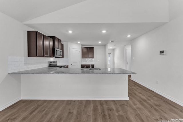 kitchen with stainless steel appliances, light stone countertops, light hardwood / wood-style flooring, and kitchen peninsula