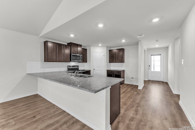 kitchen featuring light stone counters, appliances with stainless steel finishes, backsplash, dark brown cabinets, and light wood-type flooring