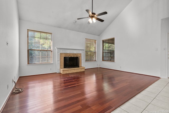 unfurnished living room featuring high vaulted ceiling, a healthy amount of sunlight, a fireplace, and light hardwood / wood-style flooring