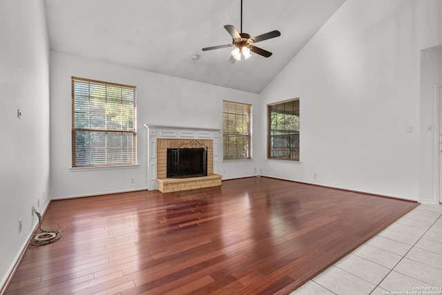 unfurnished living room with ceiling fan, wood finished floors, high vaulted ceiling, baseboards, and a fireplace with raised hearth