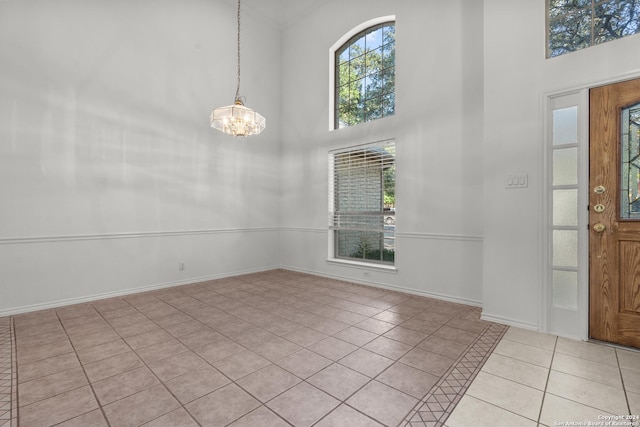 foyer entrance featuring baseboards, light tile patterned flooring, a chandelier, and a towering ceiling