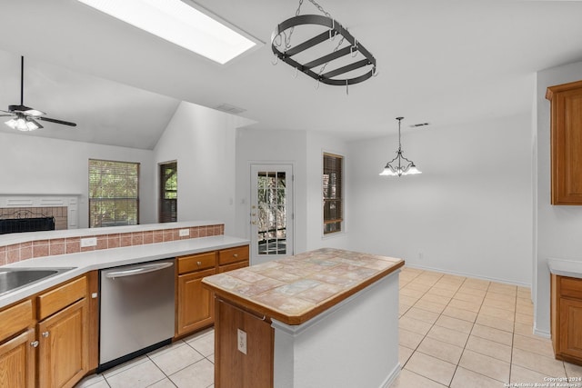 kitchen with brown cabinetry, a fireplace, dishwasher, light tile patterned floors, and ceiling fan with notable chandelier