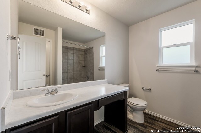 bathroom featuring wood-type flooring, vanity, a tile shower, and toilet