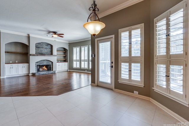 unfurnished living room featuring ceiling fan, ornamental molding, built in features, and light tile patterned floors