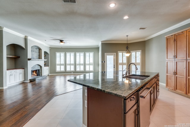 kitchen featuring sink, pendant lighting, an island with sink, dark stone counters, and built in shelves