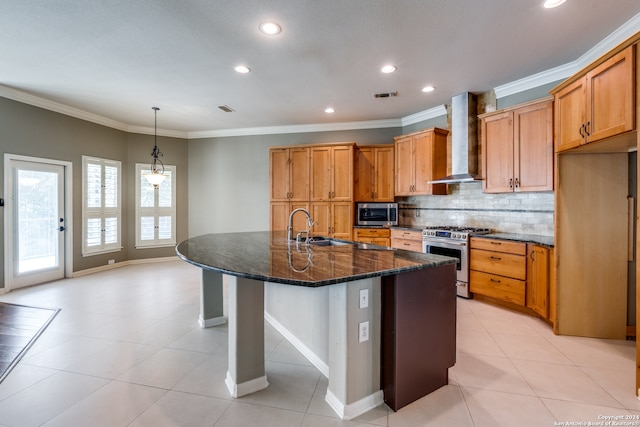 kitchen featuring stainless steel appliances, sink, wall chimney exhaust hood, dark stone counters, and a kitchen island with sink