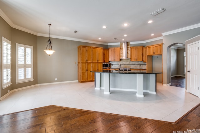 kitchen with light wood-type flooring, a center island with sink, crown molding, and wall chimney exhaust hood