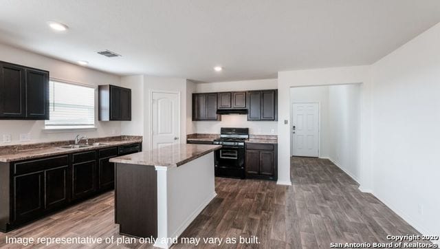 kitchen with black range with gas cooktop, a kitchen island, dark hardwood / wood-style flooring, sink, and light stone countertops