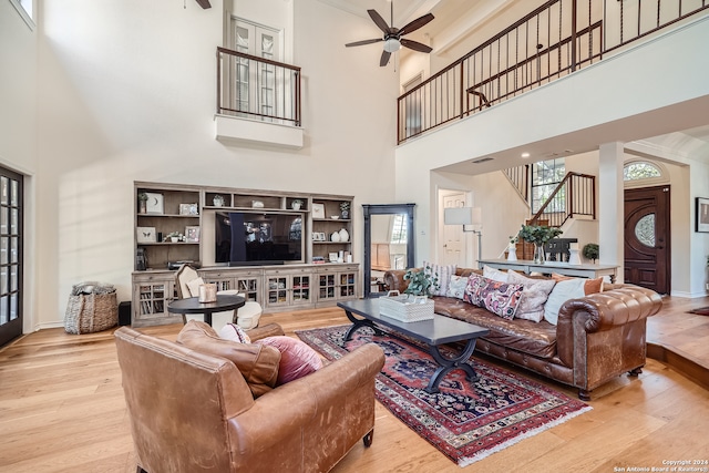 living room with ceiling fan, a towering ceiling, and light hardwood / wood-style flooring