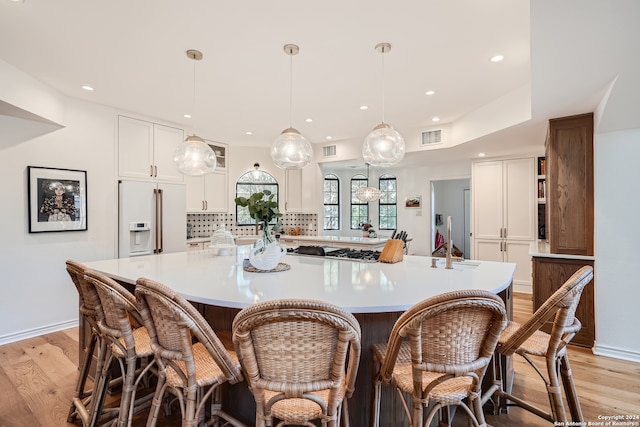 kitchen featuring tasteful backsplash, a spacious island, built in fridge, white cabinetry, and light hardwood / wood-style floors