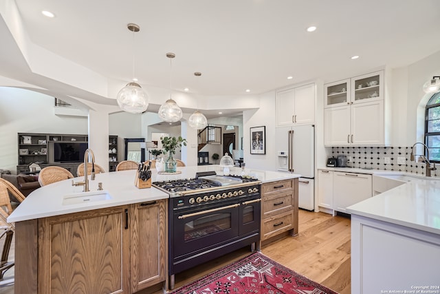 kitchen featuring an island with sink, white cabinetry, light hardwood / wood-style flooring, high quality appliances, and sink