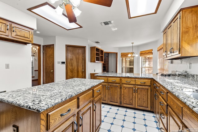 kitchen with ceiling fan with notable chandelier, decorative light fixtures, light stone countertops, kitchen peninsula, and a center island