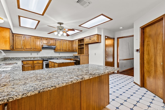 kitchen featuring a skylight, ceiling fan, stainless steel electric range oven, light stone counters, and kitchen peninsula