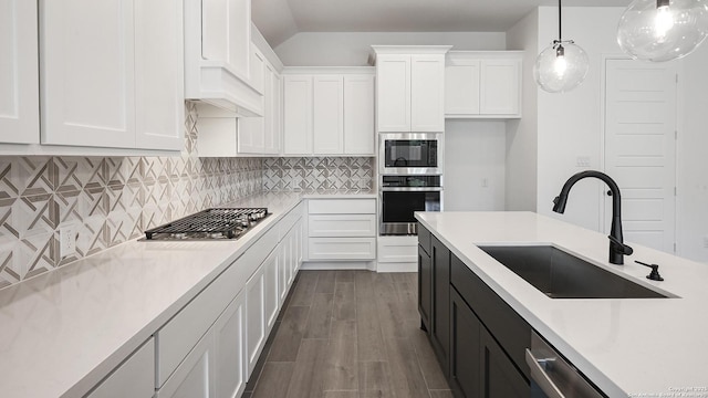 kitchen with appliances with stainless steel finishes, dark wood-type flooring, hanging light fixtures, white cabinets, and sink