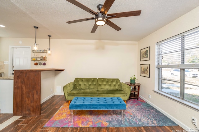 living area with ceiling fan, a textured ceiling, and dark hardwood / wood-style floors