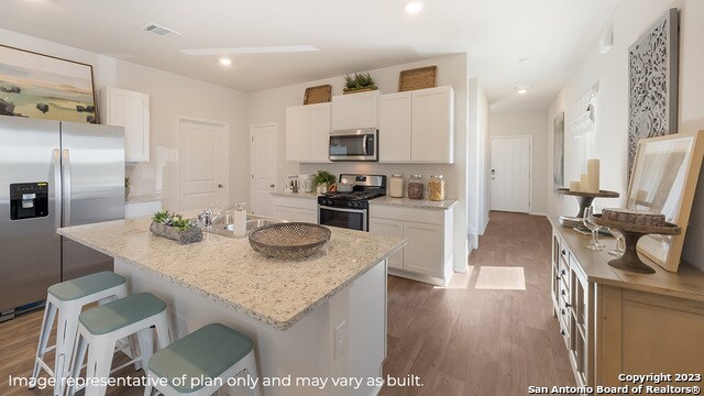 kitchen with appliances with stainless steel finishes, a sink, a breakfast bar area, white cabinetry, and wood finished floors