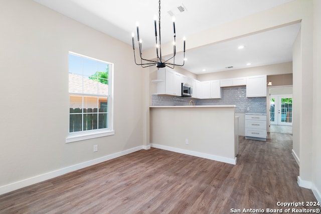 kitchen with kitchen peninsula, decorative backsplash, white cabinets, a chandelier, and dark hardwood / wood-style floors