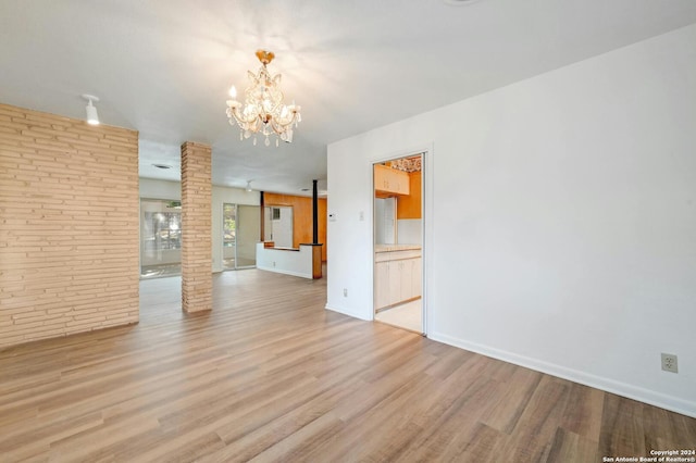 unfurnished room featuring an inviting chandelier, light hardwood / wood-style flooring, and ornate columns