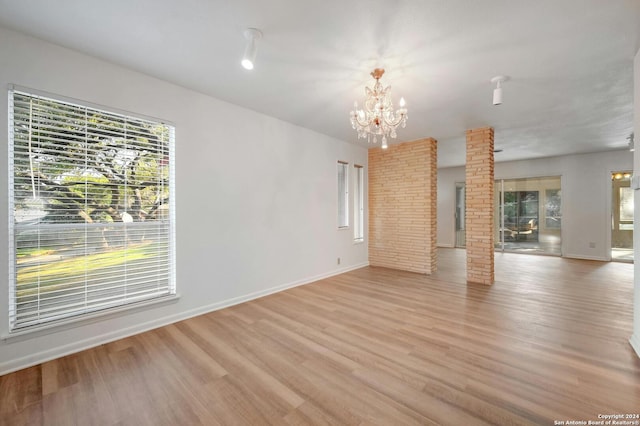 unfurnished living room featuring a notable chandelier, light hardwood / wood-style floors, and decorative columns