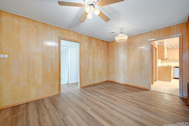 spare room featuring ceiling fan with notable chandelier, wood walls, and light hardwood / wood-style flooring