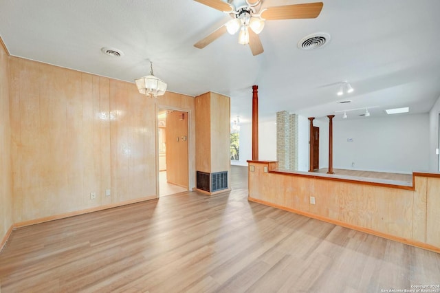 empty room with wood walls, ceiling fan with notable chandelier, and light wood-type flooring